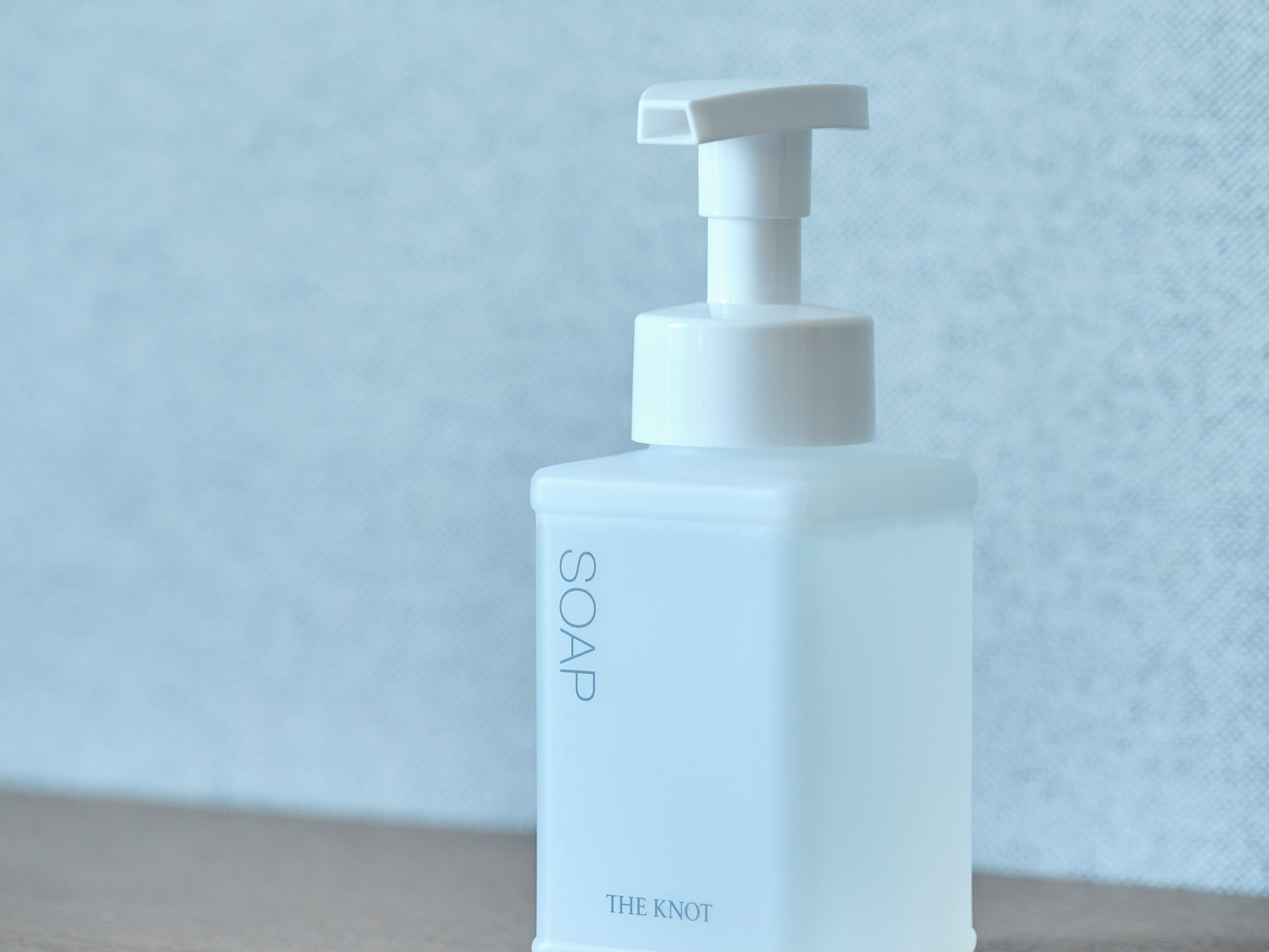 Een witte zeepdispenser met de tekst 'SOAP' en 'THE KNOT'.
