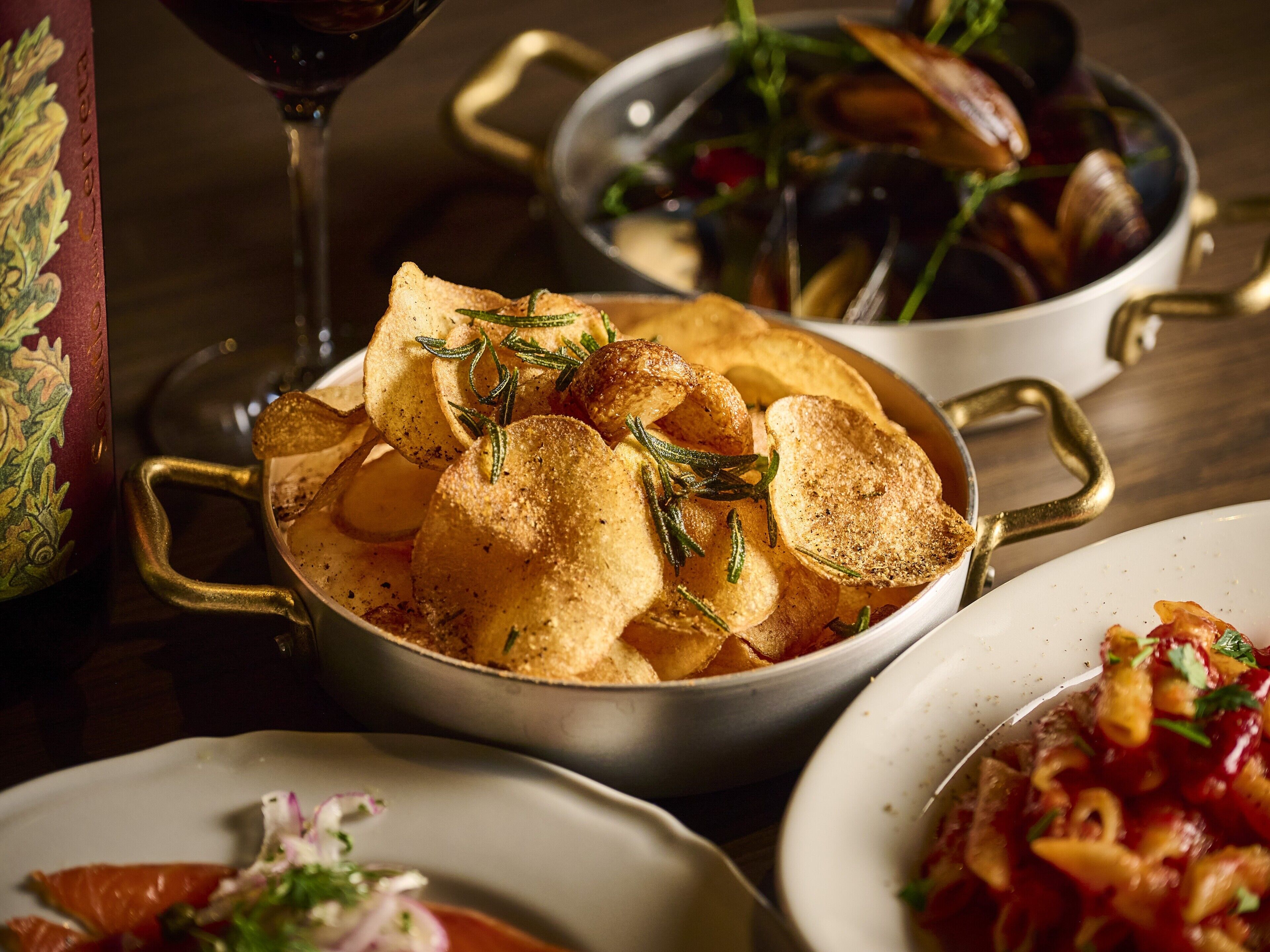 A dining table with various dishes, including a bowl of chips, a bowl of mussels, and a plate of pasta.