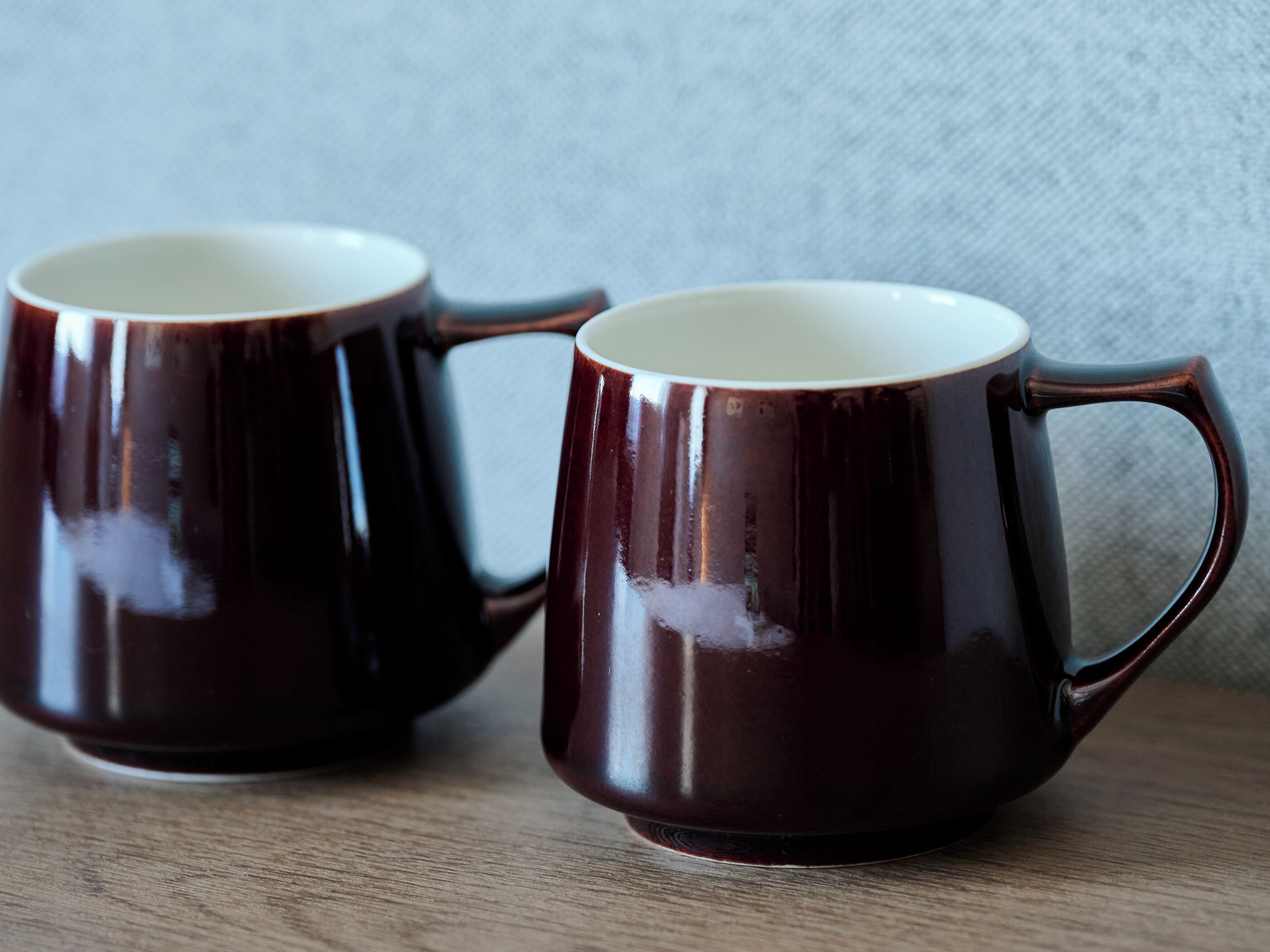 Two dark ceramic mugs with handles on a wooden surface.