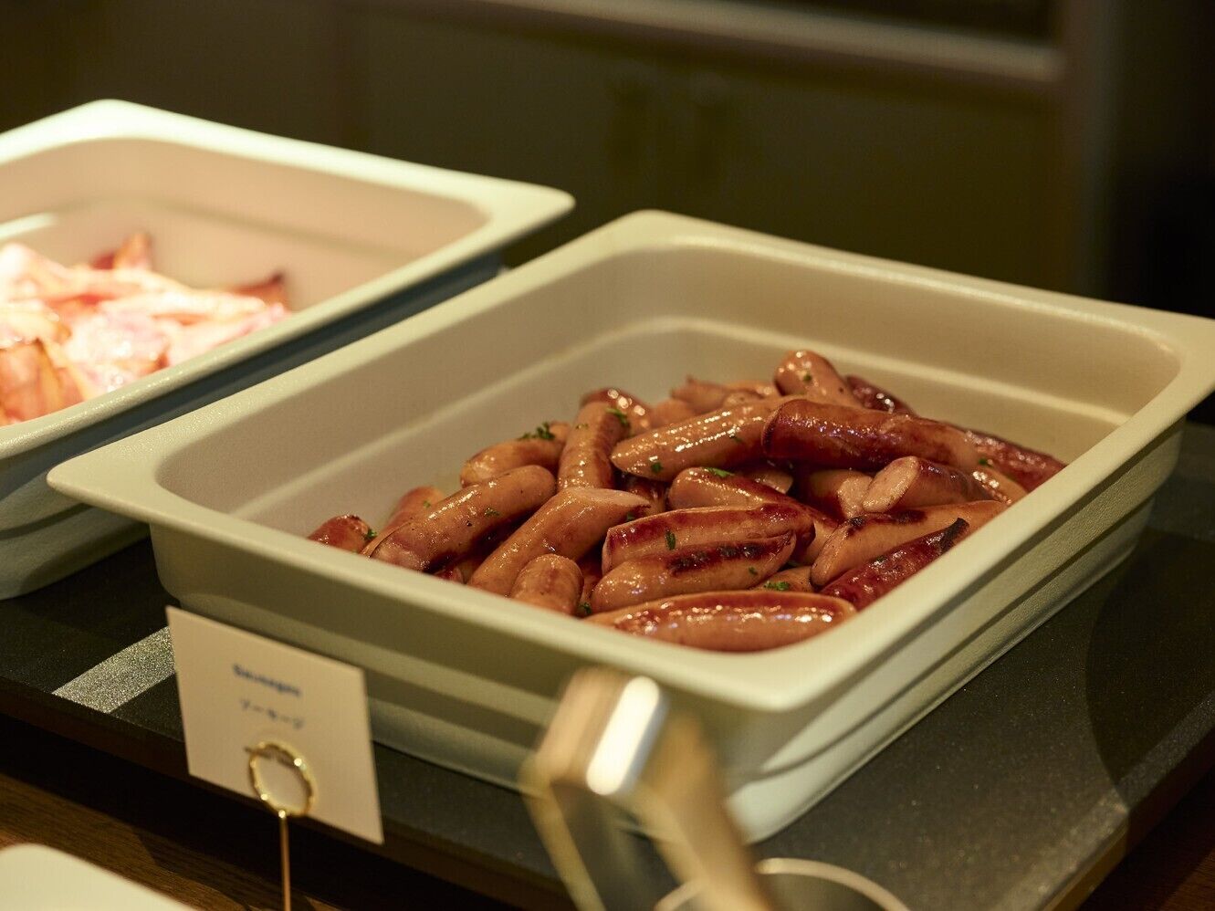 A buffet with various dishes, including sausages and a dish labeled 'Sausage.'