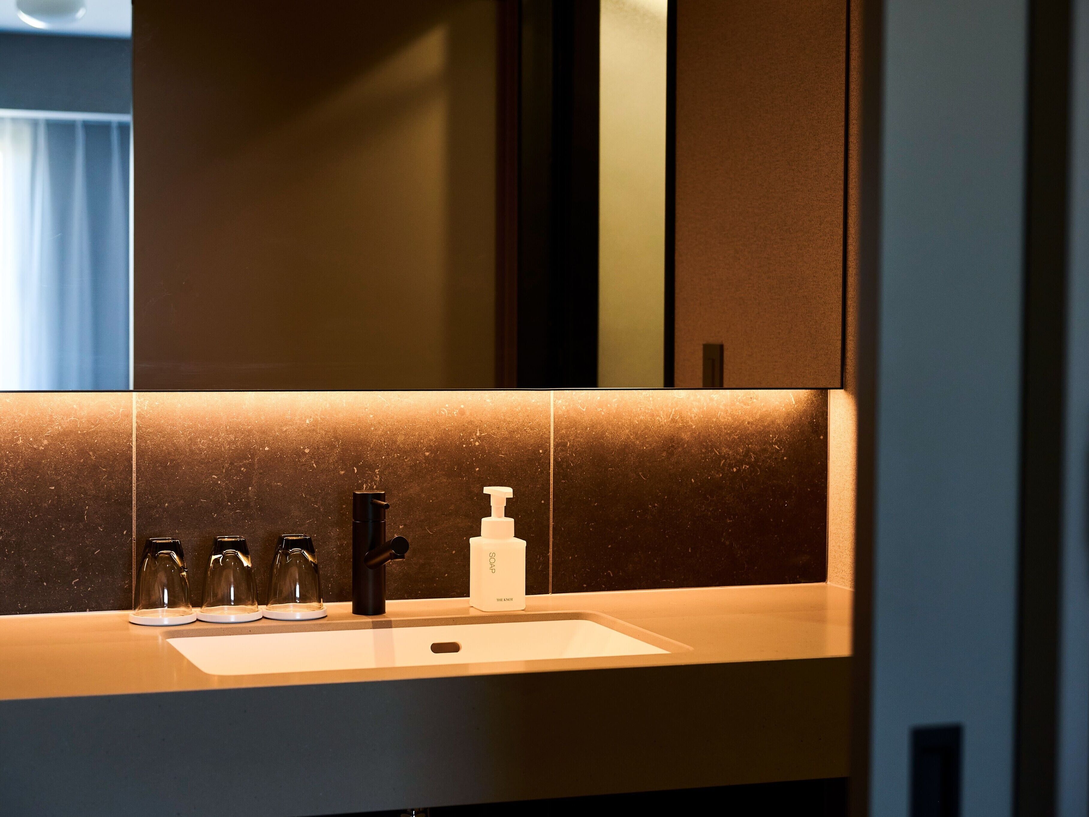 Une salle de bain moderne avec un grand miroir, un lavabo et un distributeur de savon.