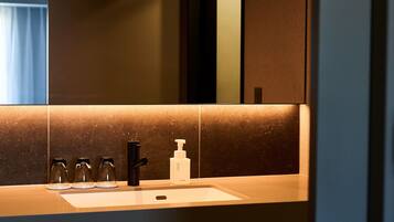 A modern bathroom with a large mirror, a sink, and a soap dispenser.