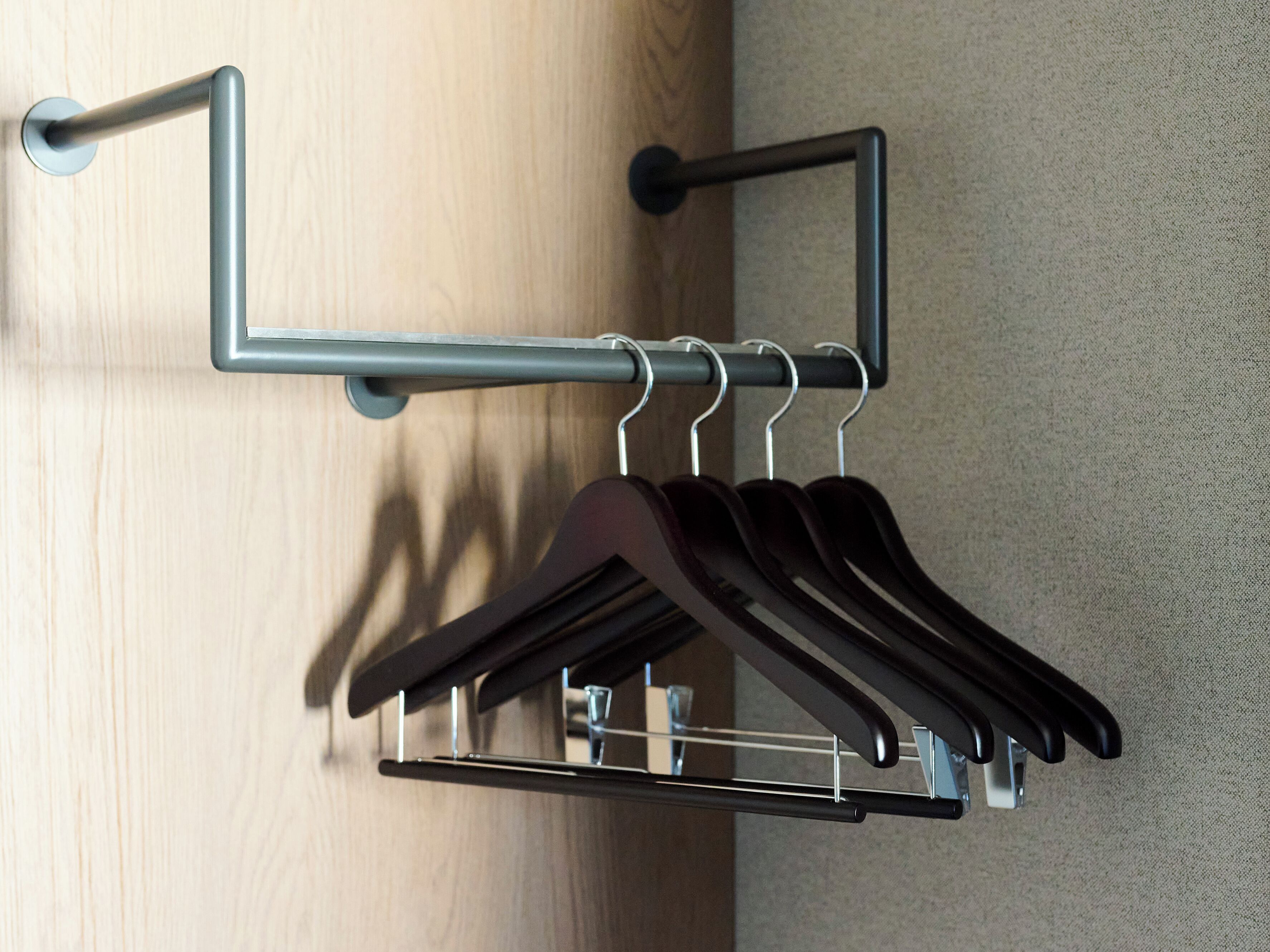 Eine Wandhalterung mit mehreren Haken, an denen schwarze Kleiderbügel hängen.