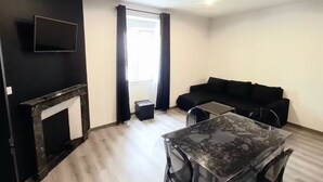 A modern living room with a black sofa, a glass dining table, and a flat-screen TV mounted on the wall. - Les suites du jardin 4 (Chaumont)