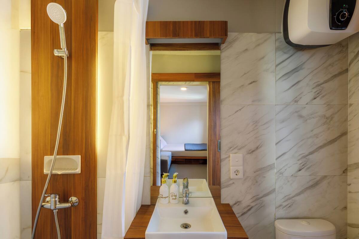 Un baño con cabina de ducha de madera, un lavamanos con dos botellas de champú y un inodoro.