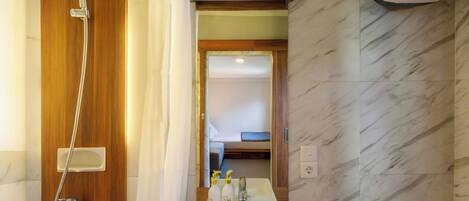 A bathroom with a wooden shower enclosure, a sink with two bottles of shampoo, and a toilet.