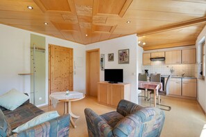 Un salon comprenant un canapé, une petite table, un téléviseur et un coin cuisine avec des placards et un évier.