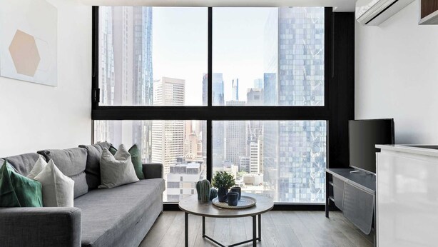 A modern living room with a grey sofa, a round coffee table, and a TV stand. - Pet-friendly Stylish 2BR Apt, Panoramic City Views (Melbourne)