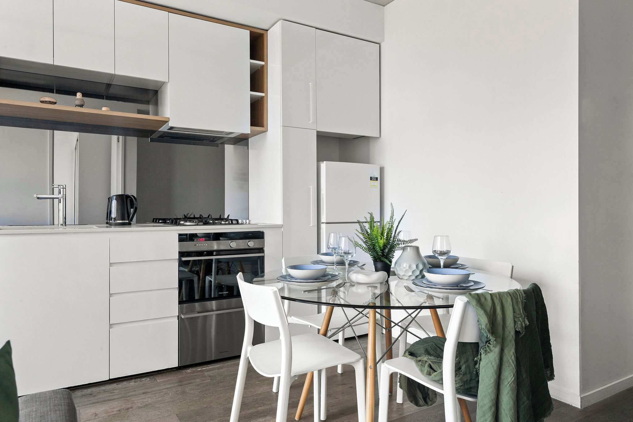Uma cozinha moderna com armários brancos, uma mesa de jantar de vidro e uma planta verde.
