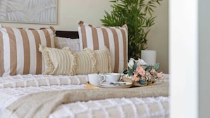 Una cama bien hecha con almohadas a rayas, una taza y platillo, y un arreglo floral sobre una bandeja.