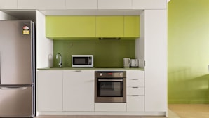 Una cocina compacta con armarios blancos, salpicadero verde, refrigerador de acero inoxidable, microondas, cafetera y horno.