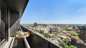 Un balcón con vistas a la ciudad, una bandeja con comida y bebida, y un cielo despejado.