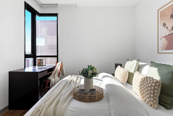 Un dormitorio con cama, escritorio, ventana y un cuadro en la pared.