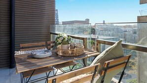 Ein Balkon mit einem Holztisch, gedeckt für ein Essen, mit Tellern, Tassen und einem Blumenkorb.