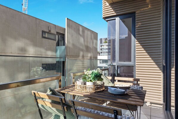 A balcony with a wooden table, chairs, and a wicker basket with flowers. - A Chic 2BR Apt Near Melbourne Uni, Free Parking (Melbourne)