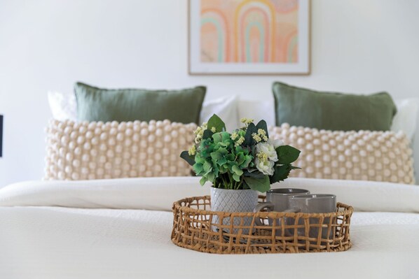 A neatly made bed with a woven tray holding a vase of flowers and candles, set against a backdrop of green pillows and a textured wall. - A Chic 2BR Apt Near Melbourne Uni, Free Parking (Melbourne)