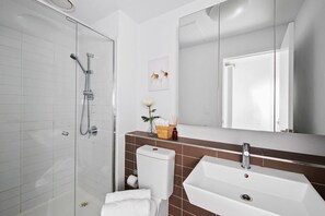 A modern bathroom with a glass-enclosed shower, a white sink, and a mirror above it. - Cozy & Modern Studio Right Next to Southern Cross (Melbourne)