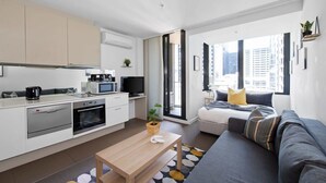 A modern apartment with a kitchenette, a dining area, a sofa, and a large window offering a city view. - Cozy & Modern Studio Right Next to Southern Cross (Melbourne)