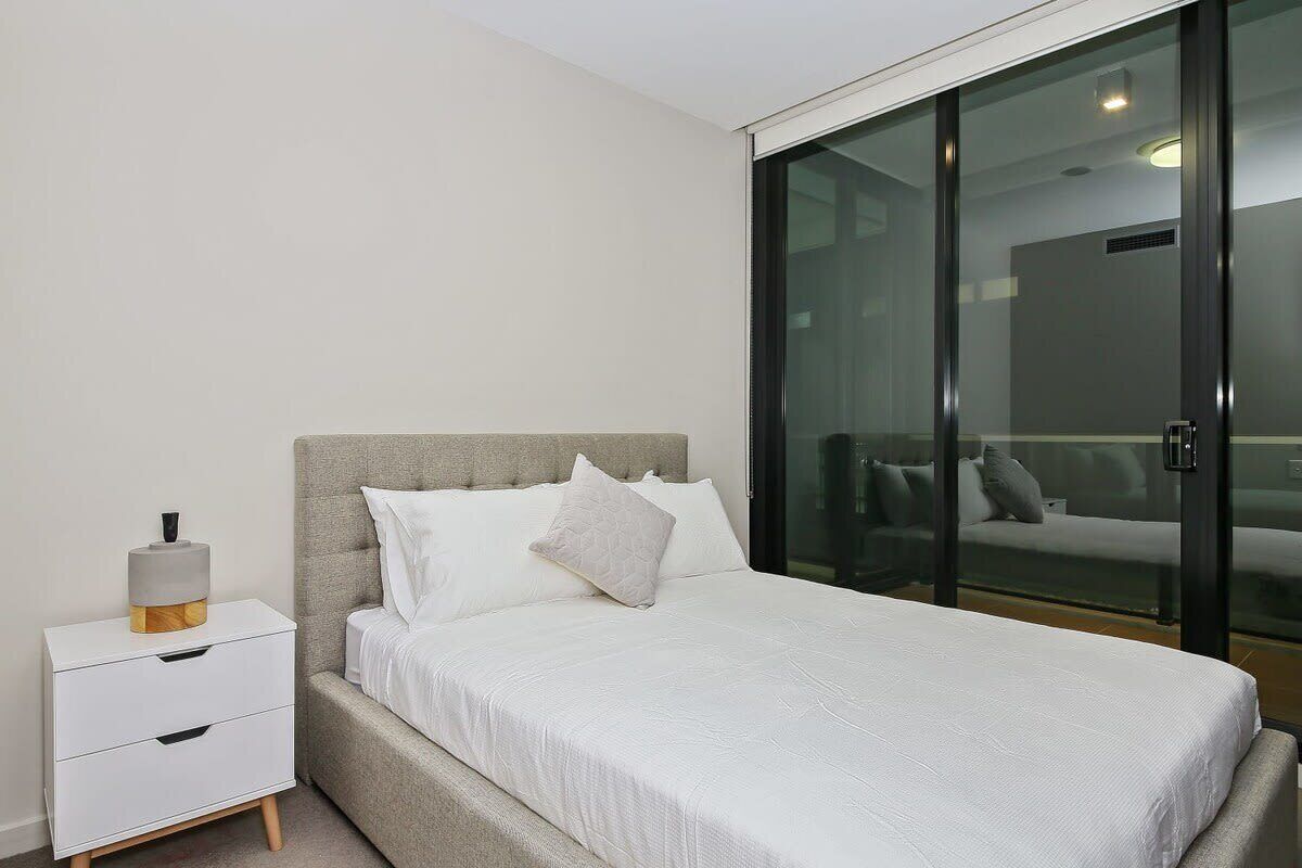 A modern bedroom with a bed, a nightstand, and a sliding glass door leading to a balcony.