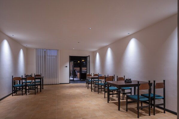 Une pièce spacieuse avec une longue table et des chaises, une porte donnant sur un autre espace et un sol carrelé.