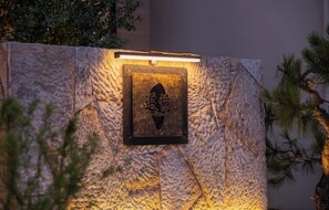 A textured stone wall with a lit sign featuring Chinese characters. - Shangri-La Memory Homestay (Deqin)