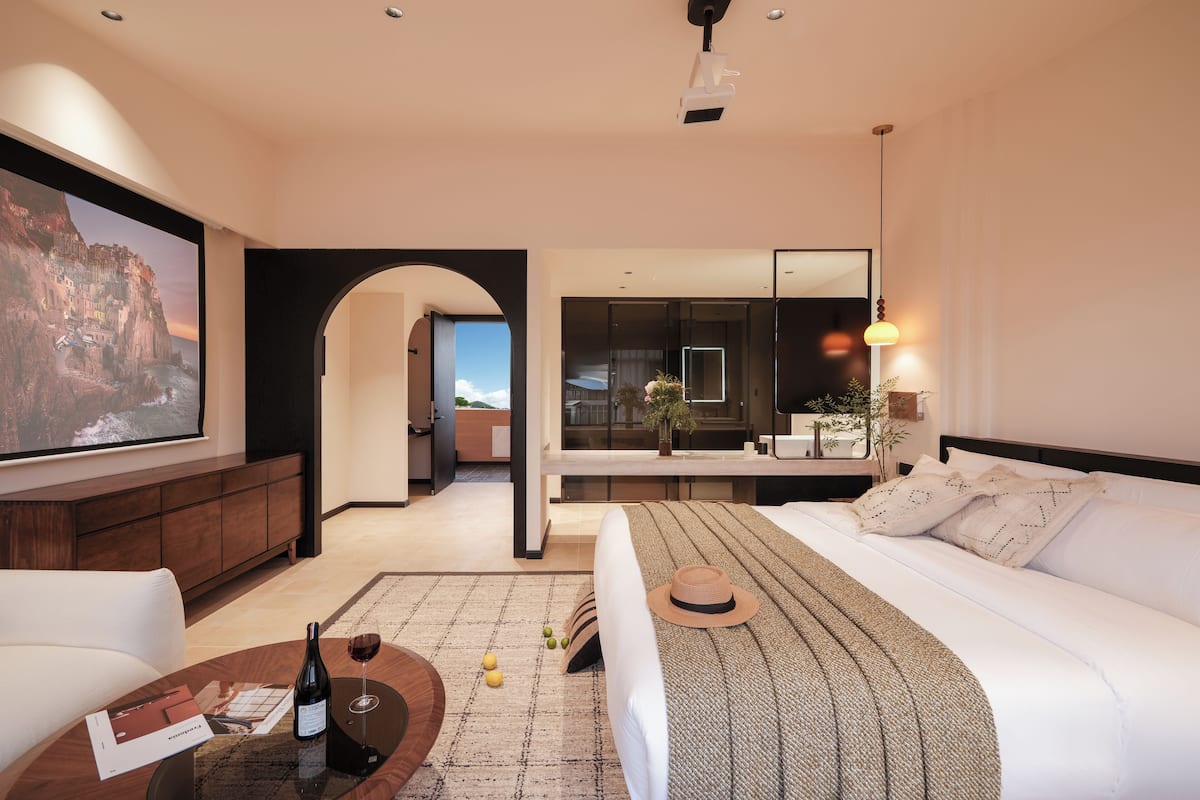 A modern hotel room with a large bed, a sitting area with a coffee table, a TV, and a view of the sea.