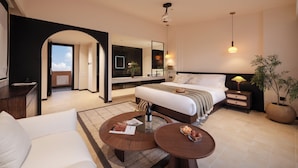 Quarto de hotel moderno com uma cama grande, área de estar com mesa de centro, escrivaninha e uma janela ampla com vista para o céu.