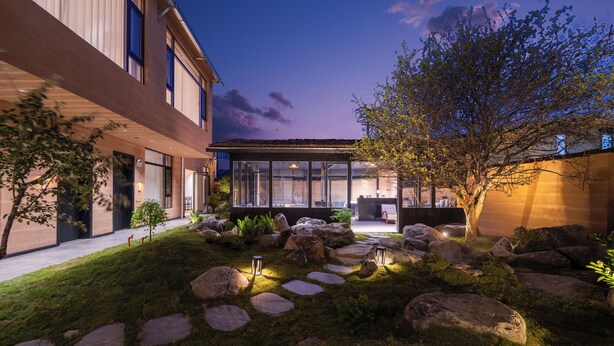 Um edifício moderno com fachada de vidro, caminho de pedra e um jardim bem cuidado com pedras e plantas.