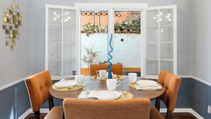 A dining room with a round table set for four, surrounded by orange chairs, with a view of a garden through a glass door.