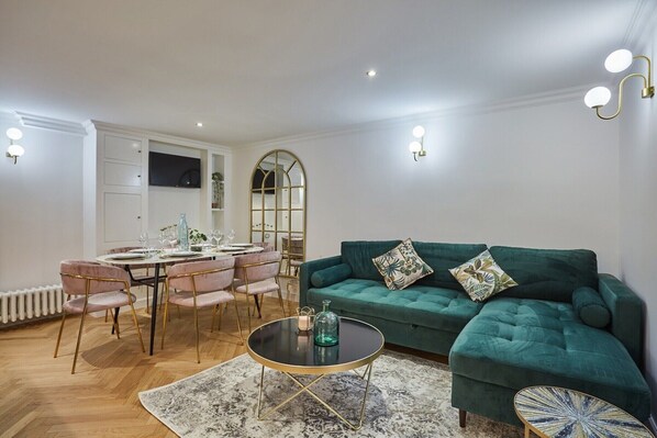 A modern living room with a green sofa, a round coffee table, and a dining area with pink chairs and a white table set.