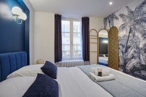 A hotel room with a large bed, a window with curtains, a wall-mounted mirror, and a tropical mural.
