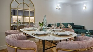 Un coin repas avec une table ronde dressée pour quatre personnes, entourée de fauteuils confortables, d’un canapé vert et d’un miroir décoratif.