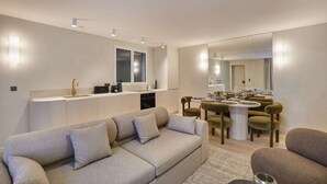 Un salon moderne avec un canapé, un coin repas avec une table dressée pour quatre personnes et une cuisine avec une fenêtre.