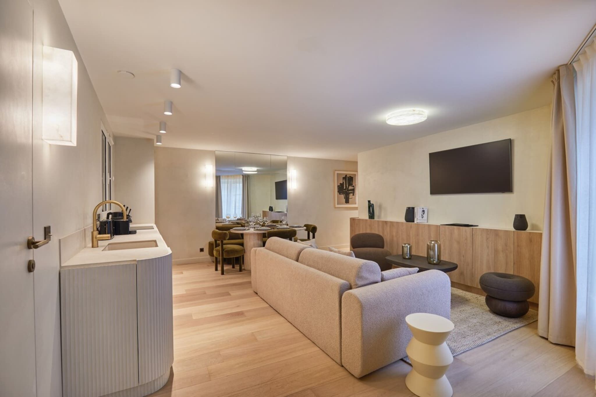 Un salon moderne avec un canapé, un coin repas avec une table et des chaises, un coin cuisine avec un évier et des placards, et un grand miroir.