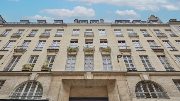 Un immeuble à plusieurs étages, doté d’une façade symétrique, de grandes fenêtres et d’une entrée centrale surmontée d’un portail en arc de cercle.