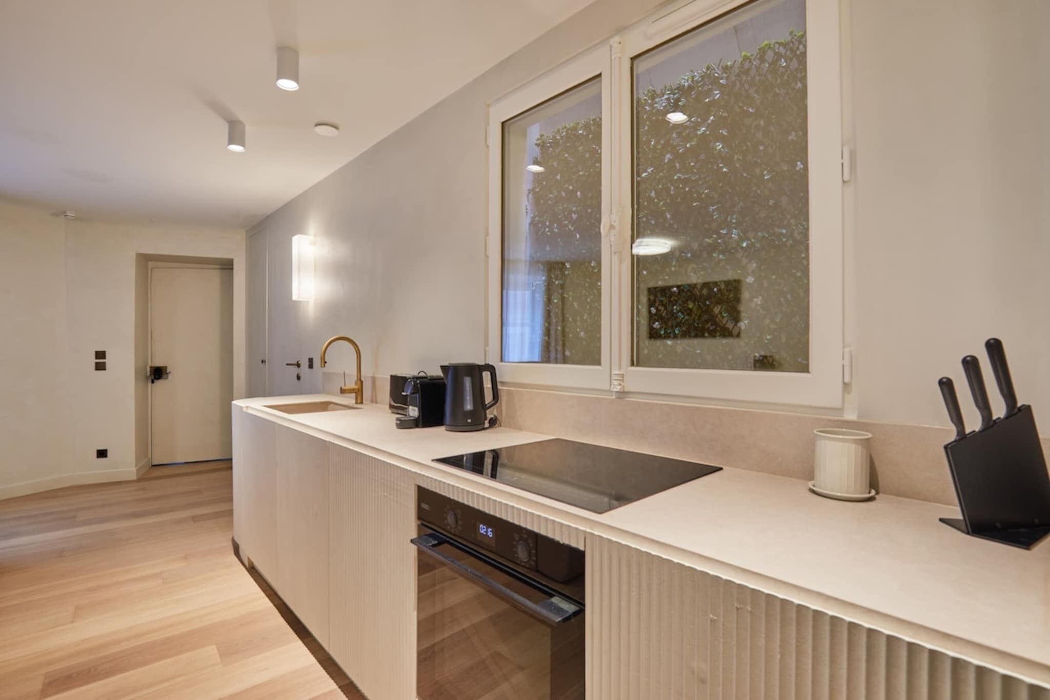 Een moderne keuken met een ingebouwde vaatwasser, een groot raam met uitzicht op bomen, en een aanrecht met een koffiezetapparaat en messen.