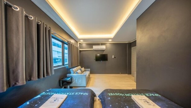 A hotel room with two beds, a sofa, a TV, and a window with curtains. - Space Station Hostel (Bangkok)