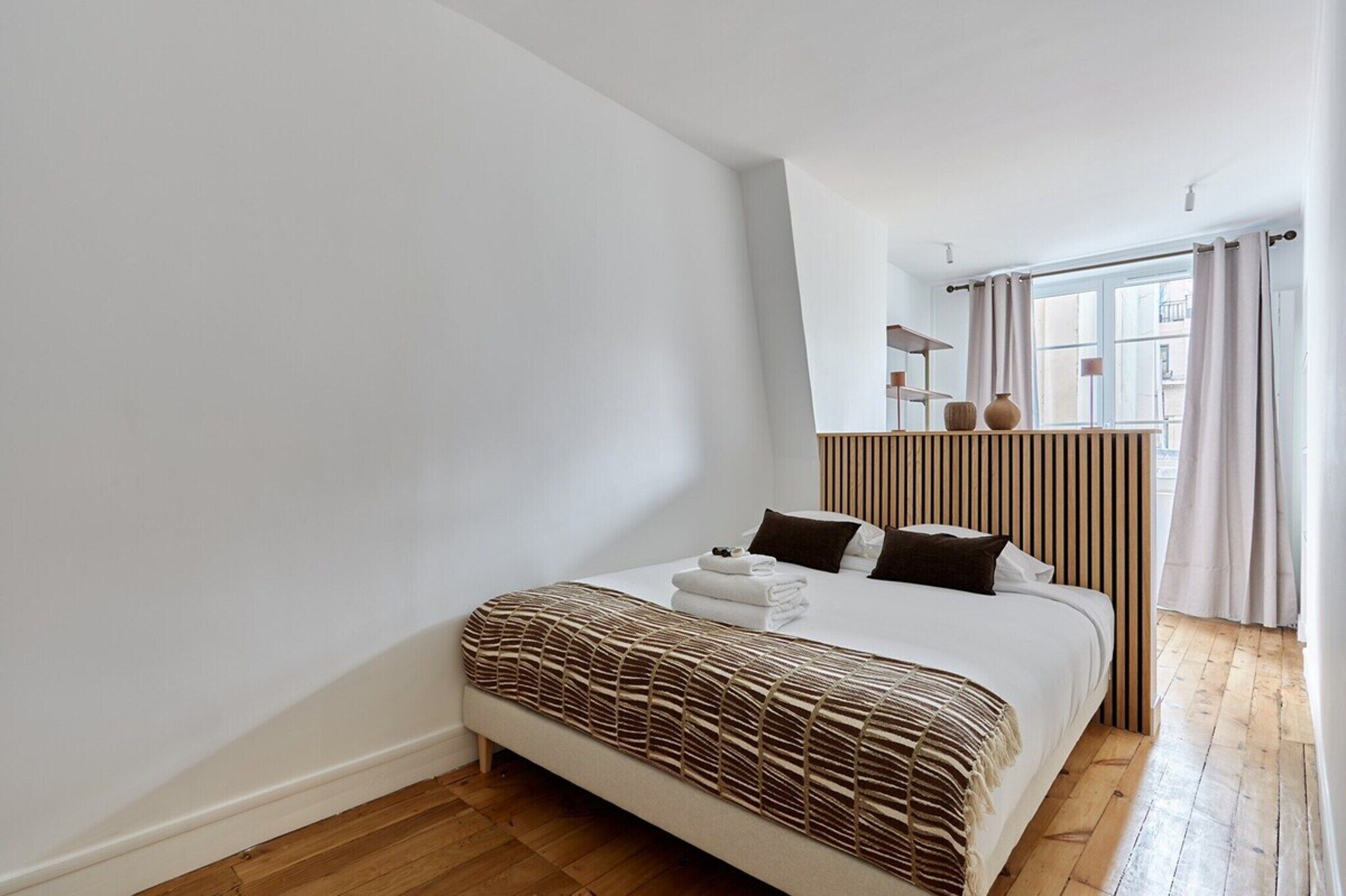 Une chambre moderne avec un grand lit, un plancher en bois, une fenêtre avec des rideaux et une vue sur la ville.