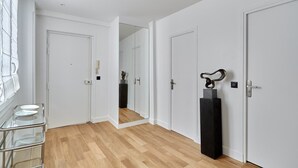 A hallway with white doors, a glass cabinet with plates, and a mirror reflecting a room with a statue. - Luxurious apartment Louvre Museum-Palais Royal (Paris)