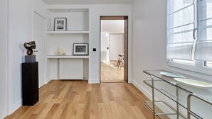 A modern interior with a wooden floor, white walls, a black sculpture, and a glass shelf with a white basin. - Luxurious apartment Louvre Museum-Palais Royal (Paris)