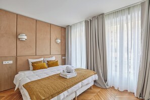 A hotel room with a large bed, wooden headboard, two wall-mounted light fixtures, and sheer curtains. - Two-bedroom flat in central Paris (Paris)