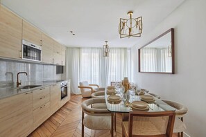 A modern kitchen with wooden cabinets, a built-in oven, and a dining area with a glass table set for four. - Two-bedroom flat in central Paris (Paris)