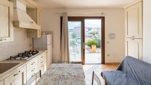 Une cuisine équipée d’une cuisinière à gaz, de placards, d’une table à manger et offrant une vue sur un espace extérieur verdoyant, accessible par une porte vitrée.