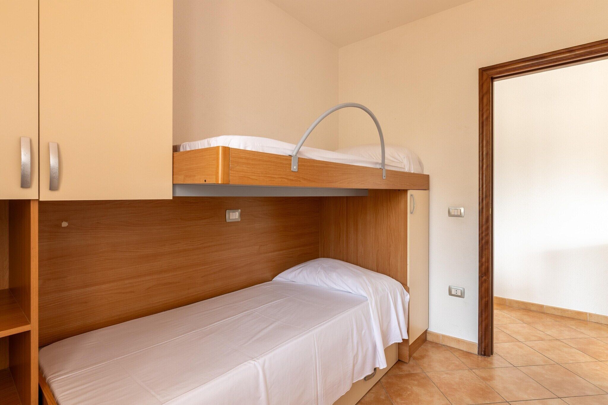 Une petite pièce avec un lit superposé et un lit simple, des murs en bois et un sol carrelé.