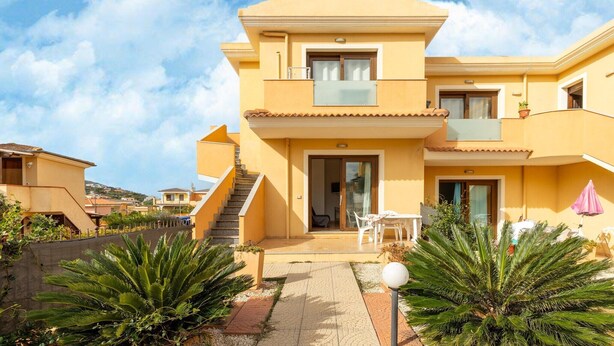 Un immeuble jaune à deux étages, doté d’un balcon, d’un escalier et d’un patio aménagé avec du mobilier d’extérieur.