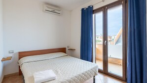 Une chambre avec un lit, une fenêtre avec des rideaux, une porte coulissante donnant sur un balcon et un climatiseur fixé au mur.