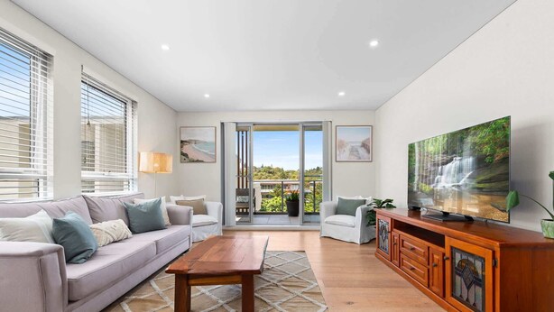 A modern living room with a sofa, coffee table, TV, and a view of a balcony with a railing. - Seaside Retreat with Parking and Balcony (Newport)