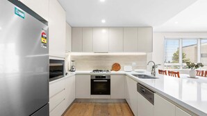 A modern kitchen with white cabinetry, a stainless steel refrigerator, a built-in oven, and a dishwasher. - Seaside Retreat with Parking and Balcony (Newport)