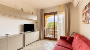 A room with a red sofa, a TV on a wooden cabinet, and a balcony with curtains.