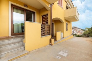 A yellow building with a balcony, a staircase, and a view of a cityscape in the background.
